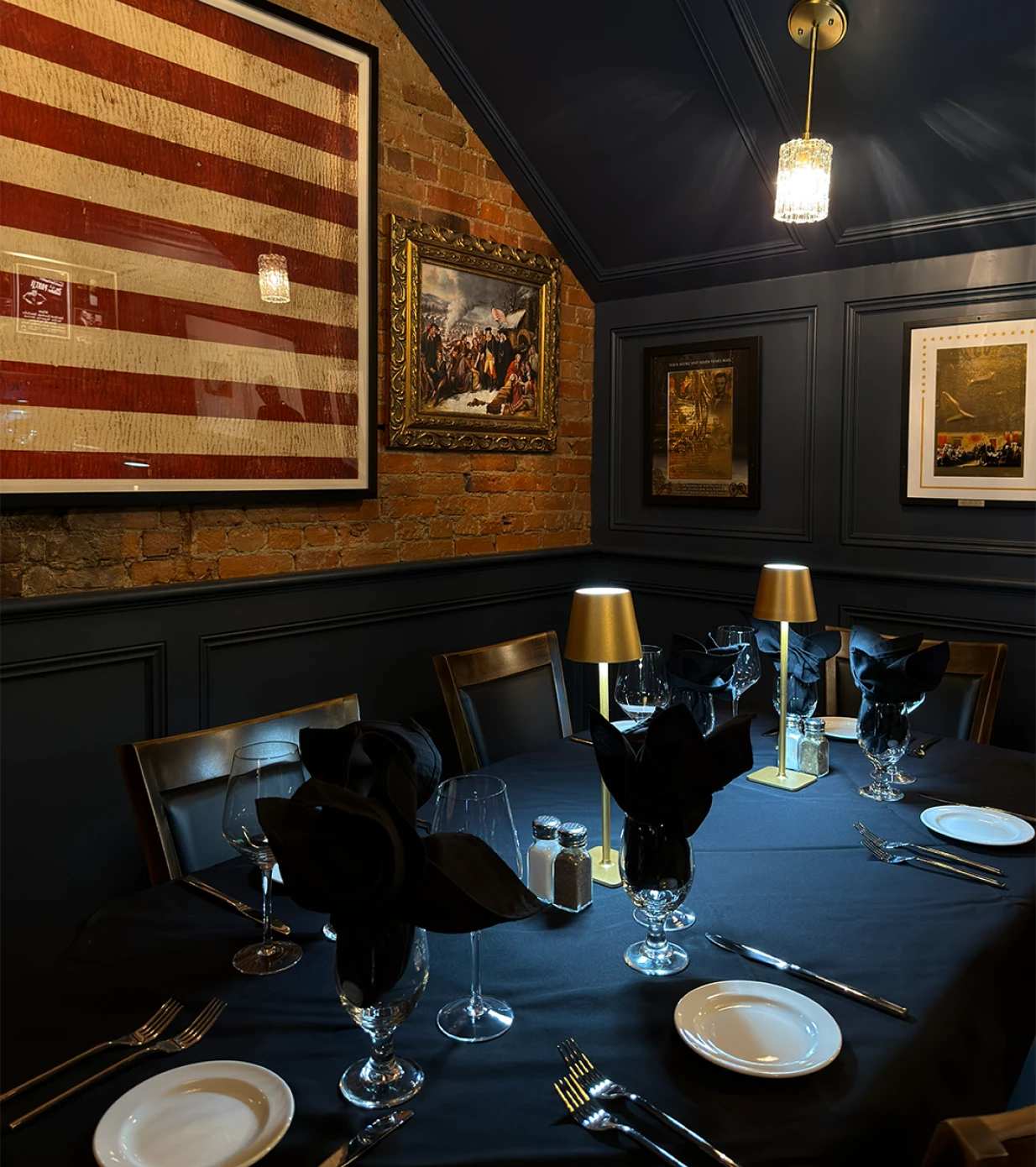 Intimate corner dining table with framed American flag, historical paintings, and warm lighting